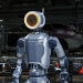 A sleek, electric Atlas robot with a ring-shaped head unit stands in a factory setting, poised to perform a task.