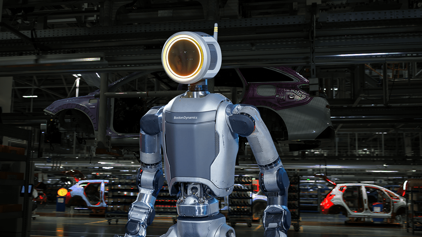 A sleek, electric Atlas robot with a ring-shaped head unit stands in a factory setting, poised to perform a task.