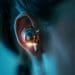 A close-up photo of a person's ear with a futuristic AI earbud glowing softly, highlighting the intimate connection between humans and AI voices.