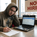 A weary crypto developer wearing an Ethereum hoodie filling out a job application inside a fast-food restaurant with a "Now Hiring" sign in the window.