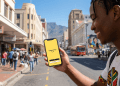 A young South African man smiling while using the Happy Pay app on a smartphone in the Cape Town CBD with Table Mountain in the background.