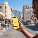 A young South African man smiling while using the Happy Pay app on a smartphone in the Cape Town CBD with Table Mountain in the background.