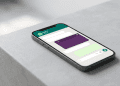 A smartphone on a minimalist grey surface displaying a WhatsApp chat interface with a single vibrant purple message bubble among standard white bubbles.
