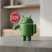 A 3D minimalist figurine of the green Android robot holding a small red stop sign, standing on a grey concrete surface with a blurred interior background.