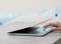 A hand interacts with a laptop trackpad amidst glowing digital waves and cloud icons, representing Googlebook's Gemini AI integration.