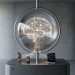 A minimalistic 3D editorial photograph illustrating Apple's agentic AI pivot, featuring a glowing digital brain in a glass sphere connected to an iPhone, Apple Watch, and MacBook on a sleek metallic pedestal with the Apple logo.