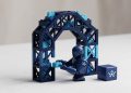 A sleek, minimalist 3D editorial photograph of a deep blue AI robot agent meticulously building a secure compliance archway using building blocks, featuring the Sumsub pixelated logo icon.