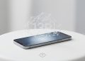 A minimalistic 3D render of a modern mobile smartphone resting on a clean white surface, with a subtle holographic network structure hovering above the screen to represent local 13B parameter LLM execution.