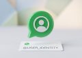 A minimalist 3D editorial graphic of a green chat bubble containing a user icon, hovering over a clean white card with '@USER_IDENTITY' to symbolise WhatsApp rolling out usernames for enhanced user privacy.