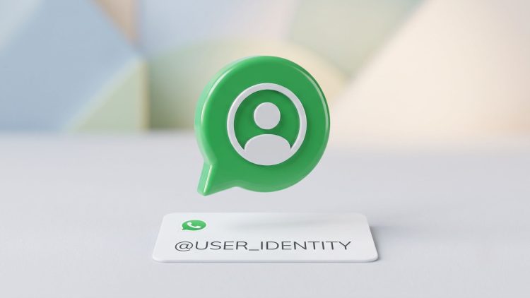 A minimalist 3D editorial graphic of a green chat bubble containing a user icon, hovering over a clean white card with '@USER_IDENTITY' to symbolise WhatsApp rolling out usernames for enhanced user privacy.